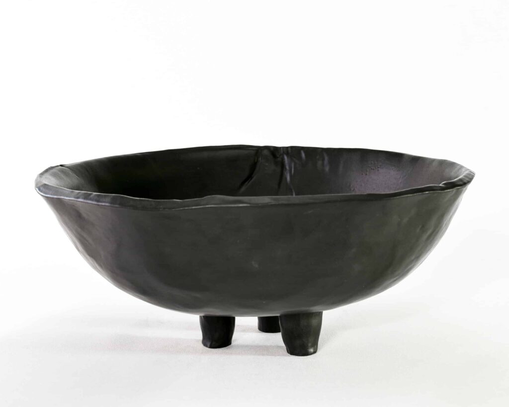 Exemplifying the "Black Magnolia" series, this matte black ceramic bowl rests on three legs; its hand-formed rim reveals organic artistry. , an original work available at MÍRAME Fine Art.