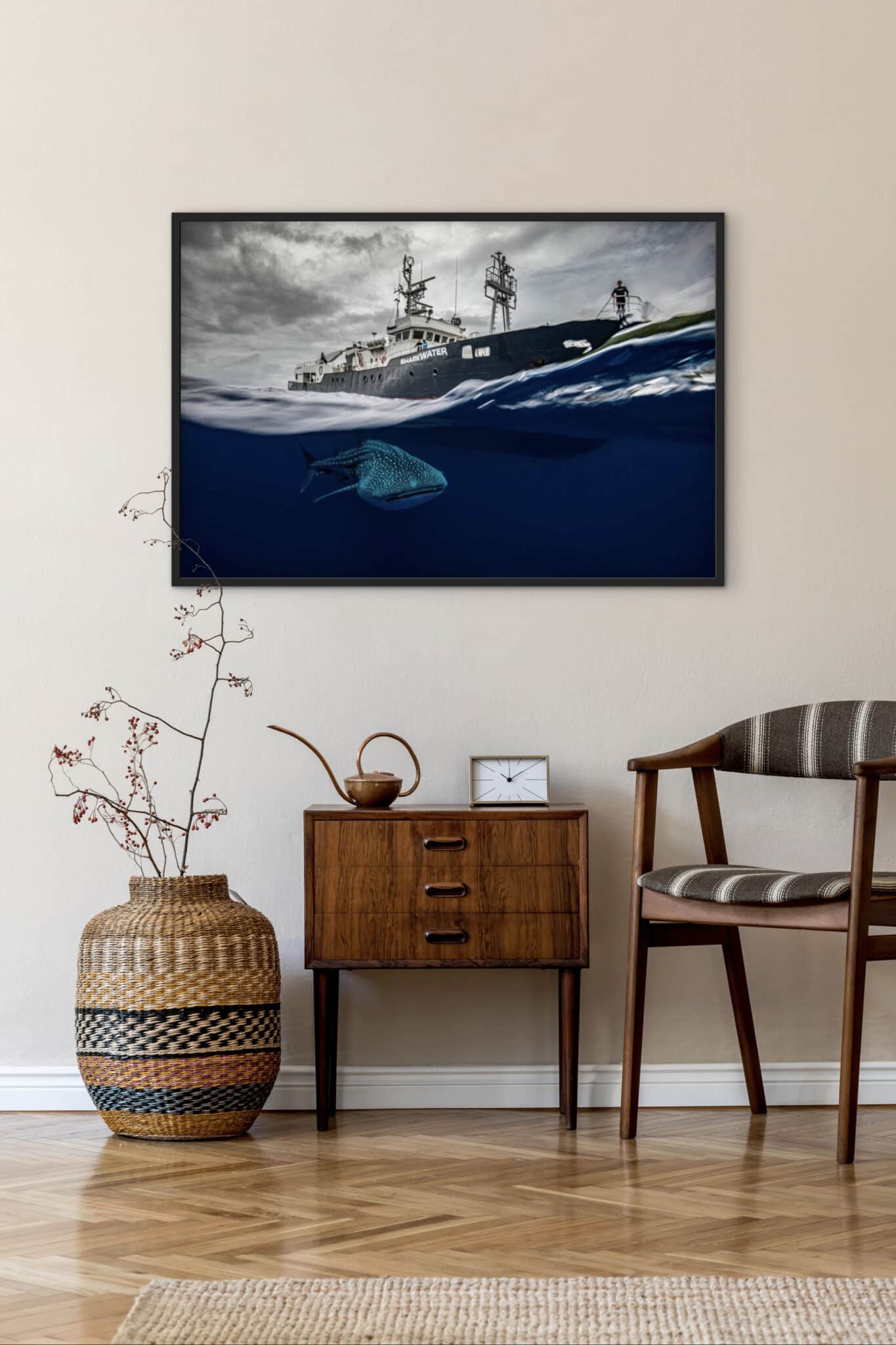 A distinguished framed photograph, “Whale shark under MV Shark Water. Cocos Island, Costa Rica,” crowns the refined interior above a wooden side table, elegantly accented with curated décor—a woven basket, timepiece, and striped chair—paying homage to United Nations World Oceans Day. , an original work available at MÍRAME Fine Art.