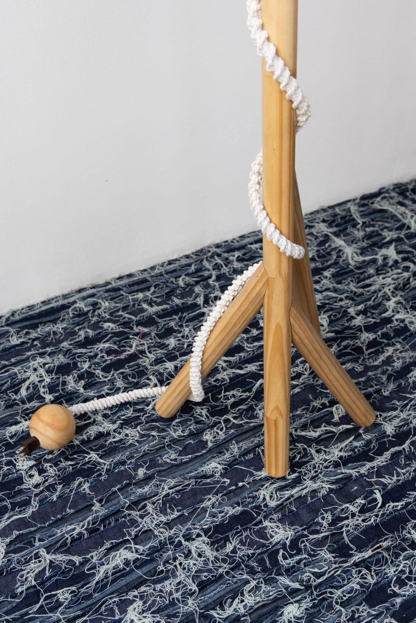 A refined light wood tripod, titled "Olimpia," is poised on rich blue fabric, its leg entwined with rope near an Art Deco vase. , an original work available at MÍRAME Fine Art.