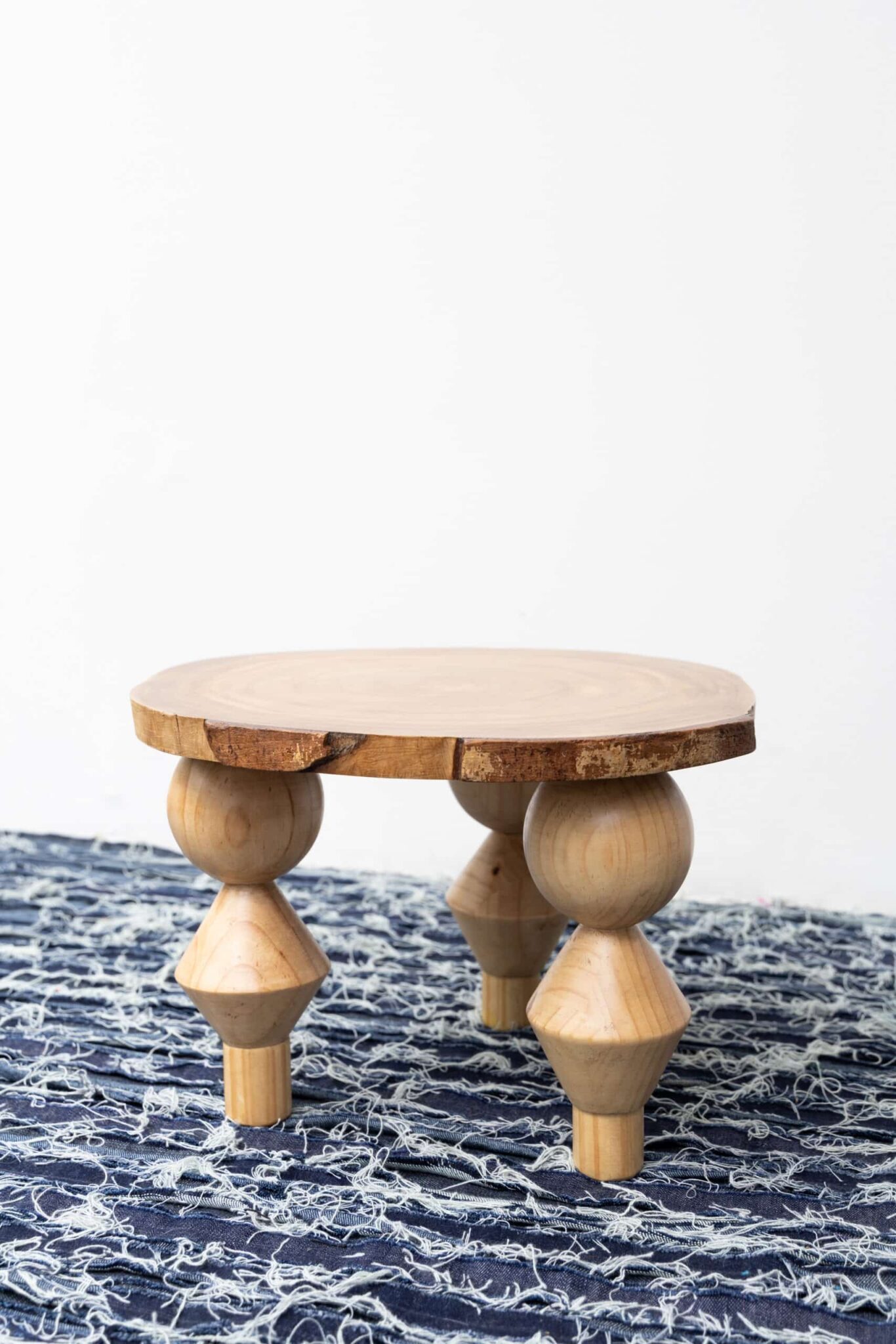Olimpia: a refined, round wooden table with geometric tripod legs, atop a patterned blue rug, crowned by an art deco vase. , an original work available at MÍRAME Fine Art.