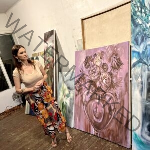 Olga Anaskina in her studio with Olga Anaskina painting in the background.