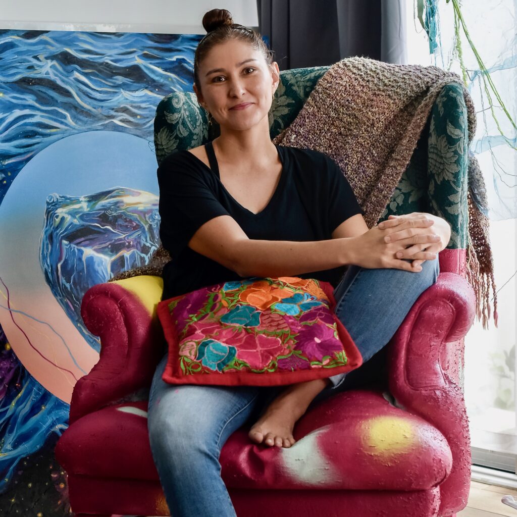 Portrait of Costa Rican artist Karla Herencia sitting on a chair in front of her work, in her studio.