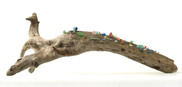 A wooden trunk sculpture of driftwood with colourful pieces of plastic embedded in the wood.