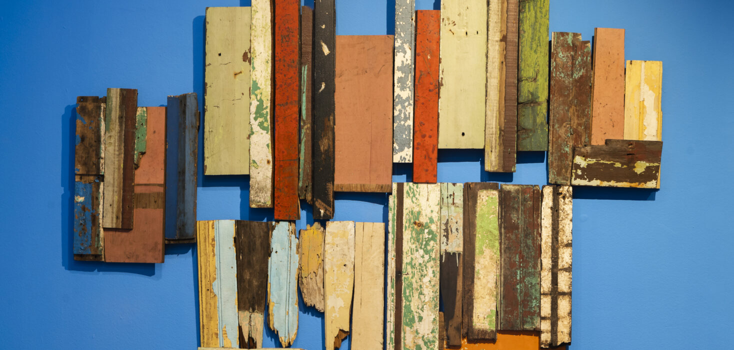 Sculptural artwork formed of different coloured pieces of wood arranged on a blue wall. Exemplifying Ivannia Lasso urban decay.