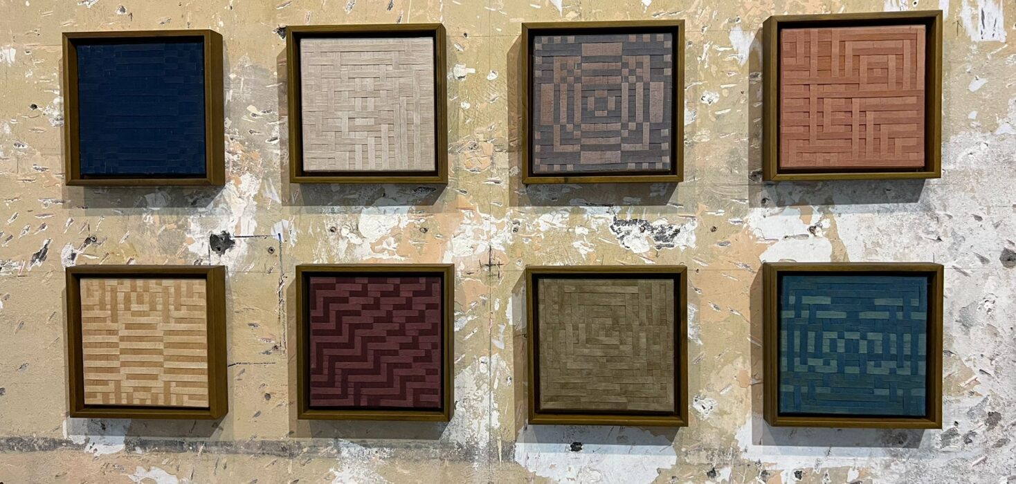 Eight small colourful textile artworks hanging on a wall, featured in Más Allá Del Índigo at San José's MADC.