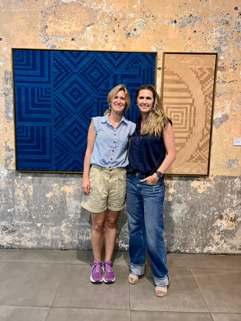 Two women standing in front of a blue and beige artwork.