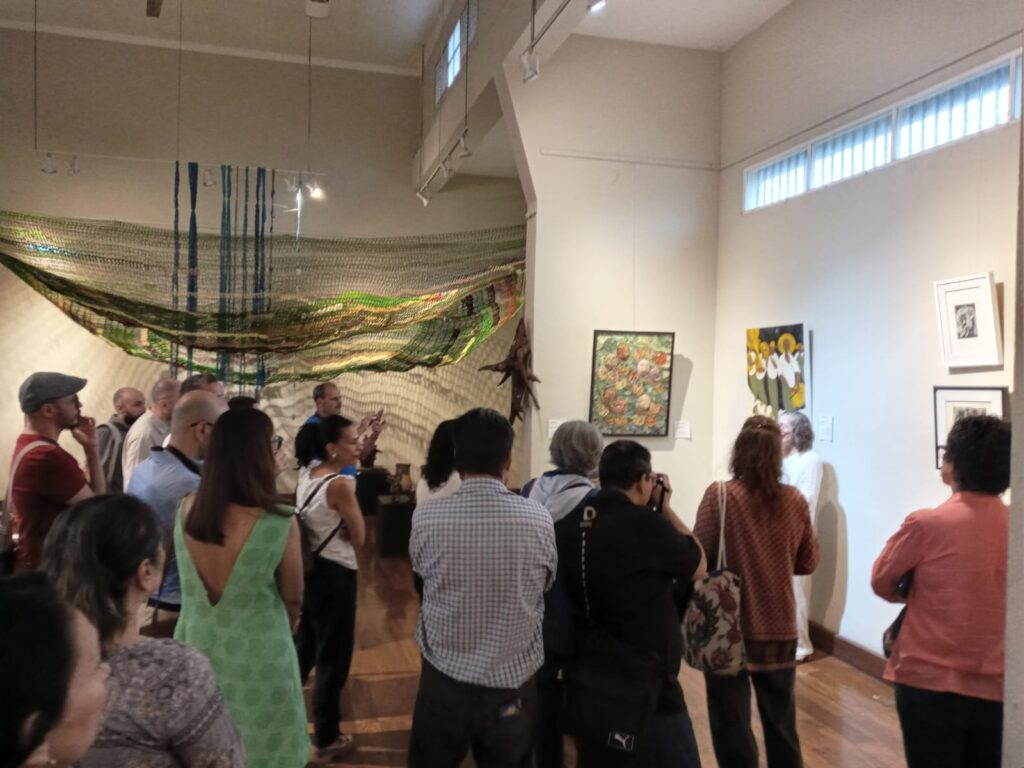 People stood in the exhibition space of a Guanacaste Exhibition, looking at artwork and listening to an artist talking.