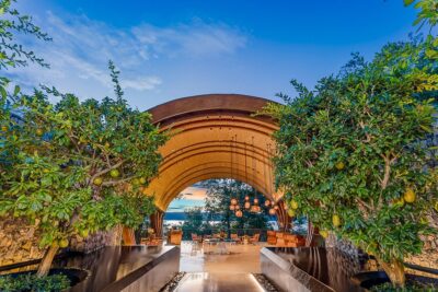 Image of a hotel entryway, looking down a walkway to tables and chairs and the ocean beyond. To advertise Andaz Art Week.