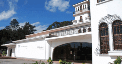 View of the outside of a white, imperial style building with blue sky ahead and trees behind. Museum housing the Salón Nacional de Artes Visuales