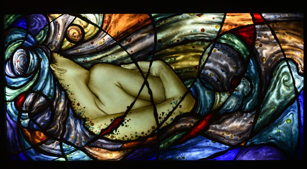 Colorful and bright abstract stained glass festuring a figure emerging from the colours of blue, orange and turquoise.