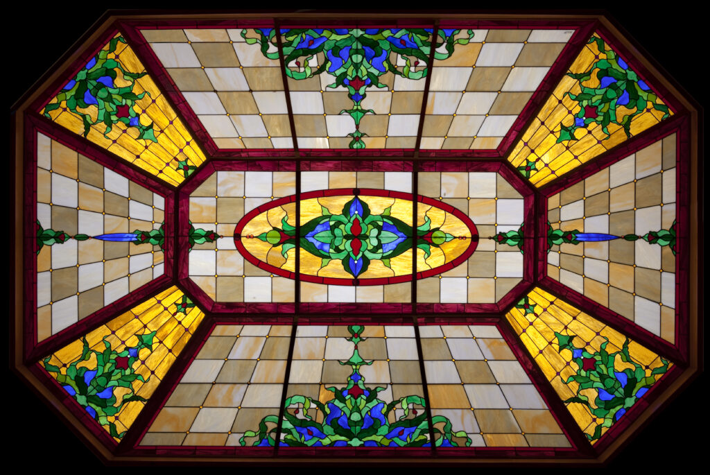 Yellow stained glass with art deco style patterns and neutral colours either side of the yellow shapes.