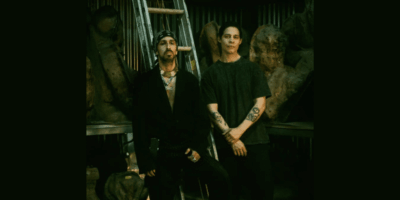 Dark portrait of artists Pablo Mejias and Gregory Fage, standing side-by-side in front of a ladder and sculptures. The image coincides with their show of Latin American Dark Figurative Art in November 2025