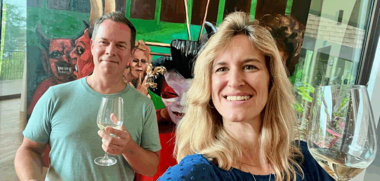 A man and a woman hold up a glass of champagne in front of a masquerade painting, during Andaz Art Week Costa Rica.