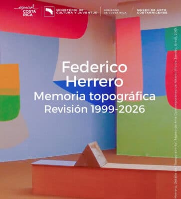 Federico Herrero, Memoria topográfica. Revisión 1999–2026, exhibition poster. Background image shows a colourful immersive installation with large geometric forms in red, blue, green, orange, and lavender across floor and walls, with a terracotta triangular sculptural element in the foreground. Museum of Costa Rican Art, San José, Costa Rica.