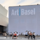 Visitors convene before Art Basel’s striking white facade, engaging in lively discourse and casual strolls amid a convivial ambiance. Illustrating a feature on Art Basel and Latin American Art